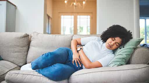 Woman on a couch, clutching her stomach in discomfort, illustrating the overlapping bloating and cramping symptoms of IBS and SIBO.