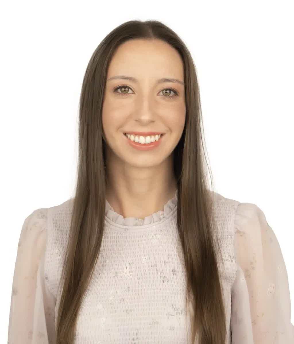 Smiling young woman with long straight brown hair wearing a light pink textured blouse against a white background