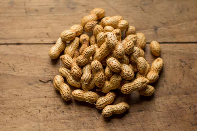 A pile of unshelled peanuts on a wooden surface.