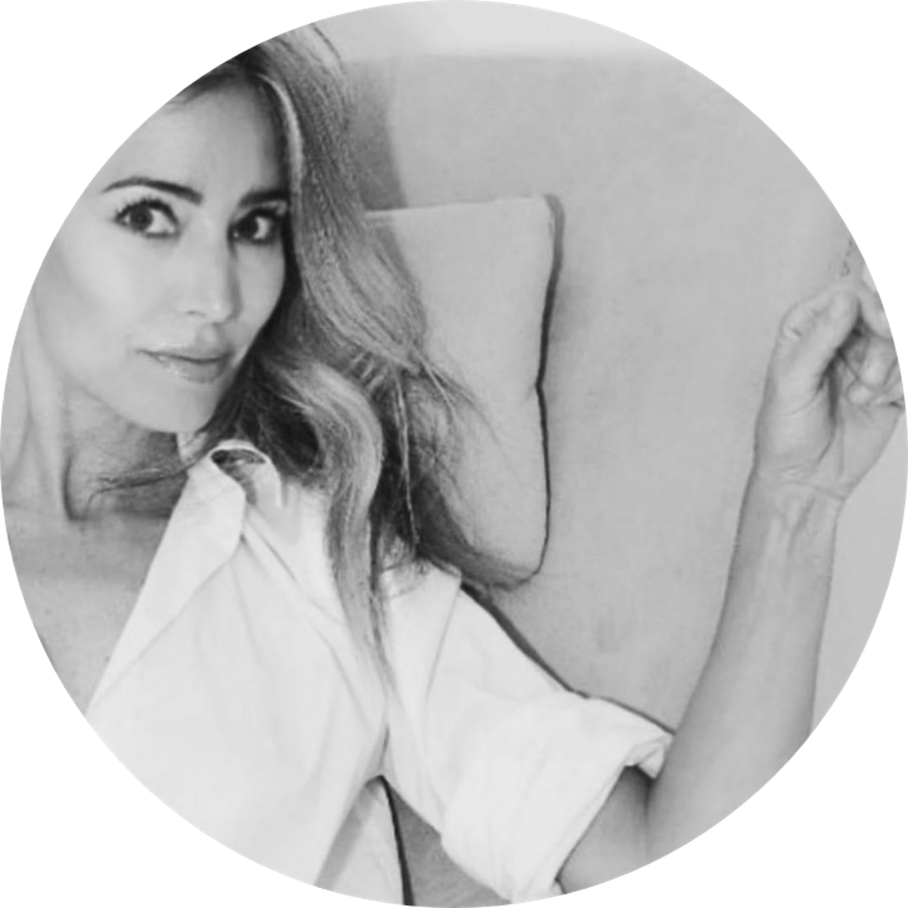 Smiling woman with blonde hair wearing a black wide-brim hat and black top, sitting against a dark backdrop.