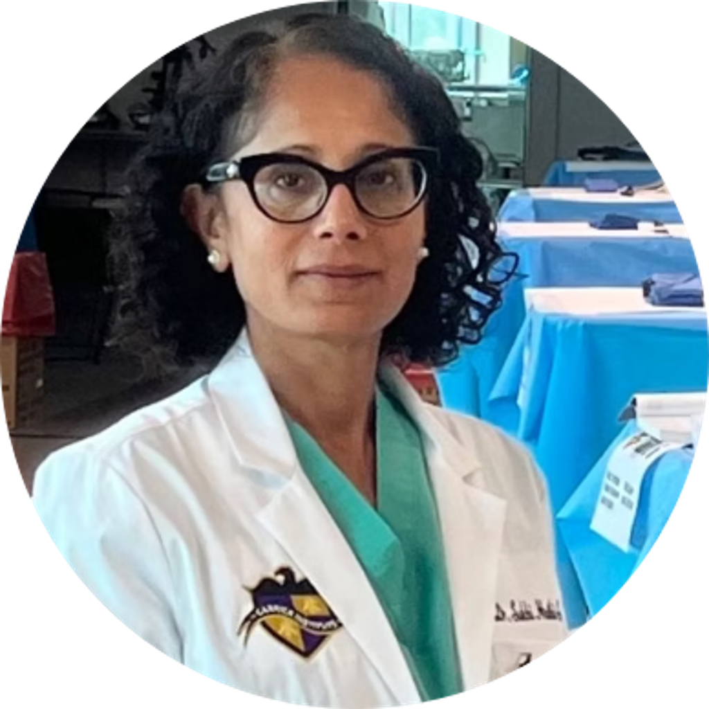 Smiling woman with blonde hair wearing a black wide-brim hat and black top, sitting against a dark backdrop.