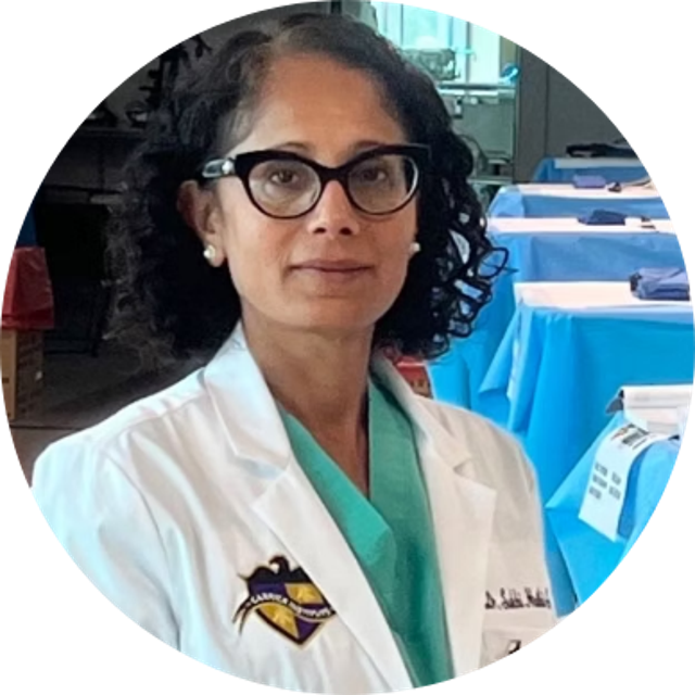 Smiling woman with blonde hair wearing a black wide-brim hat and black top, sitting against a dark backdrop.