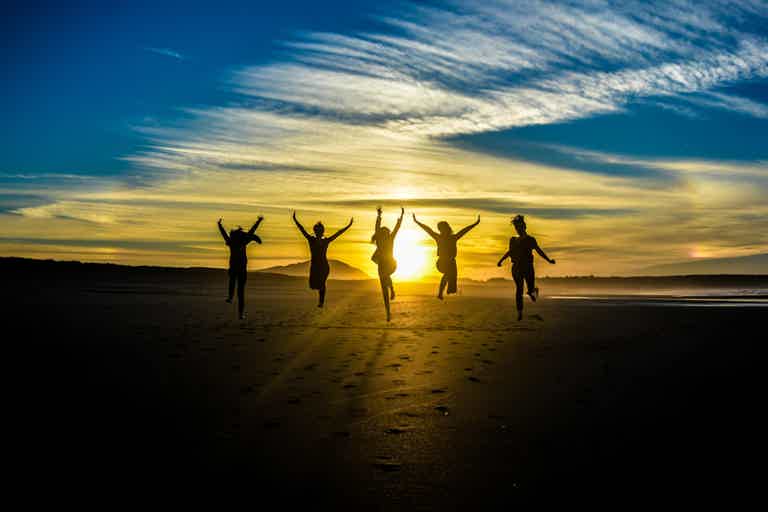 Group of friends jumping on a beach at sunset, silhouettes against bright sky.