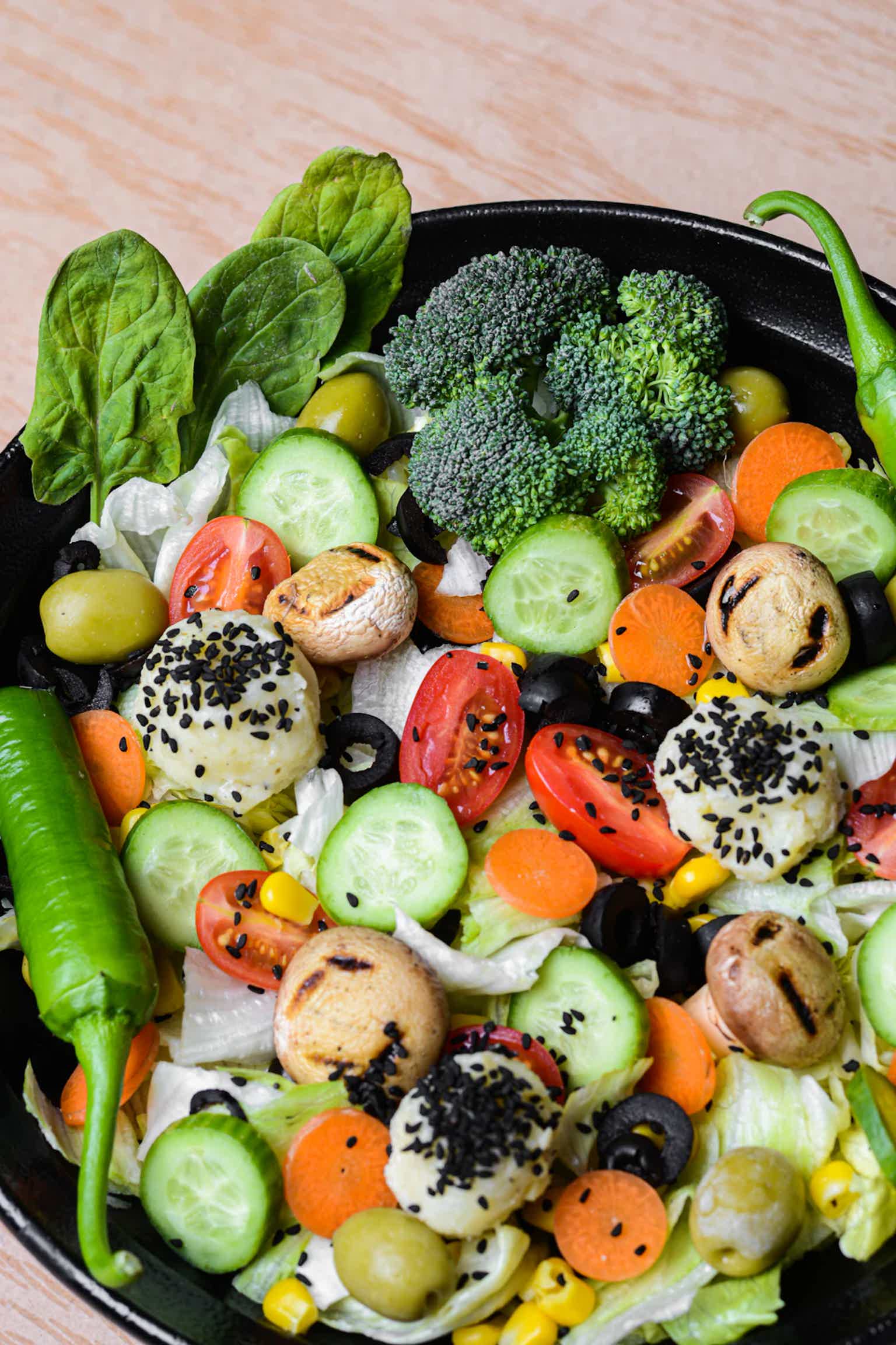 Colorful sautéed vegetables including broccoli, cucumbers, carrots, tomatoes, olives, corn, granny, and greens in a pan.