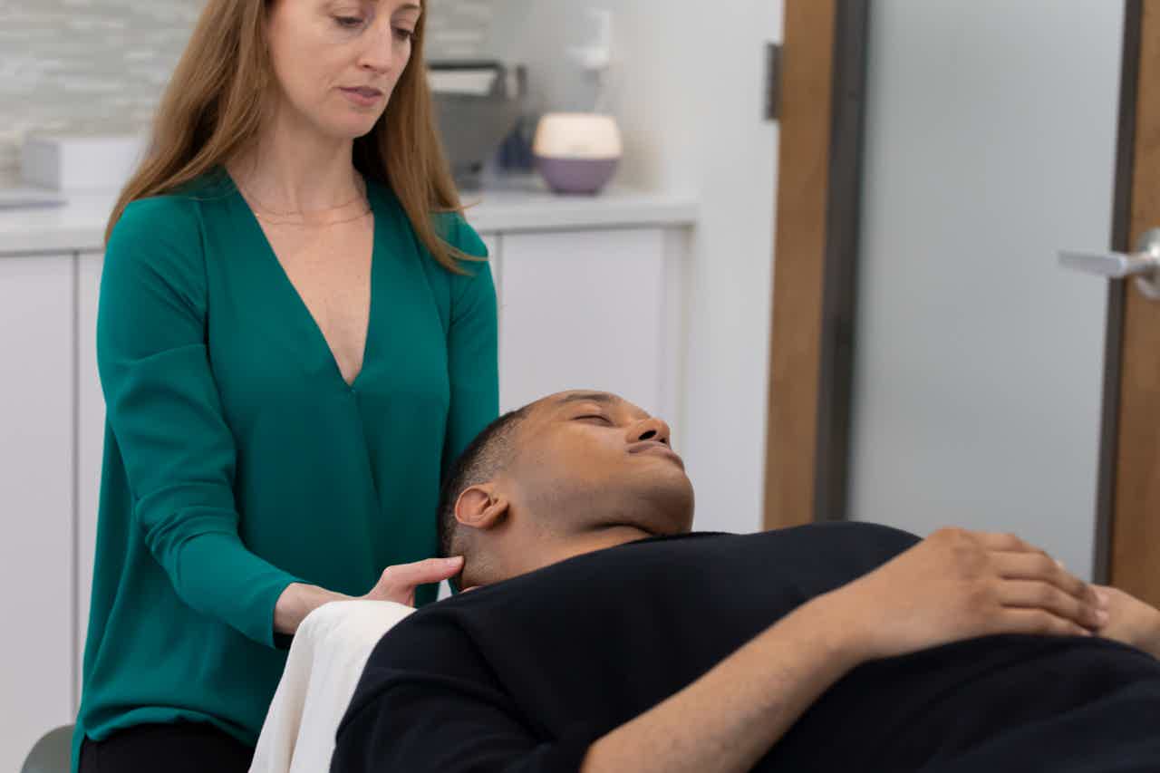 Massage Therapist performs bedside assessment, gently holding a patient’s head