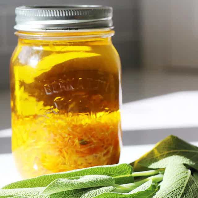Jar of golden honey with grated zest inside; sage leaves in foreground.