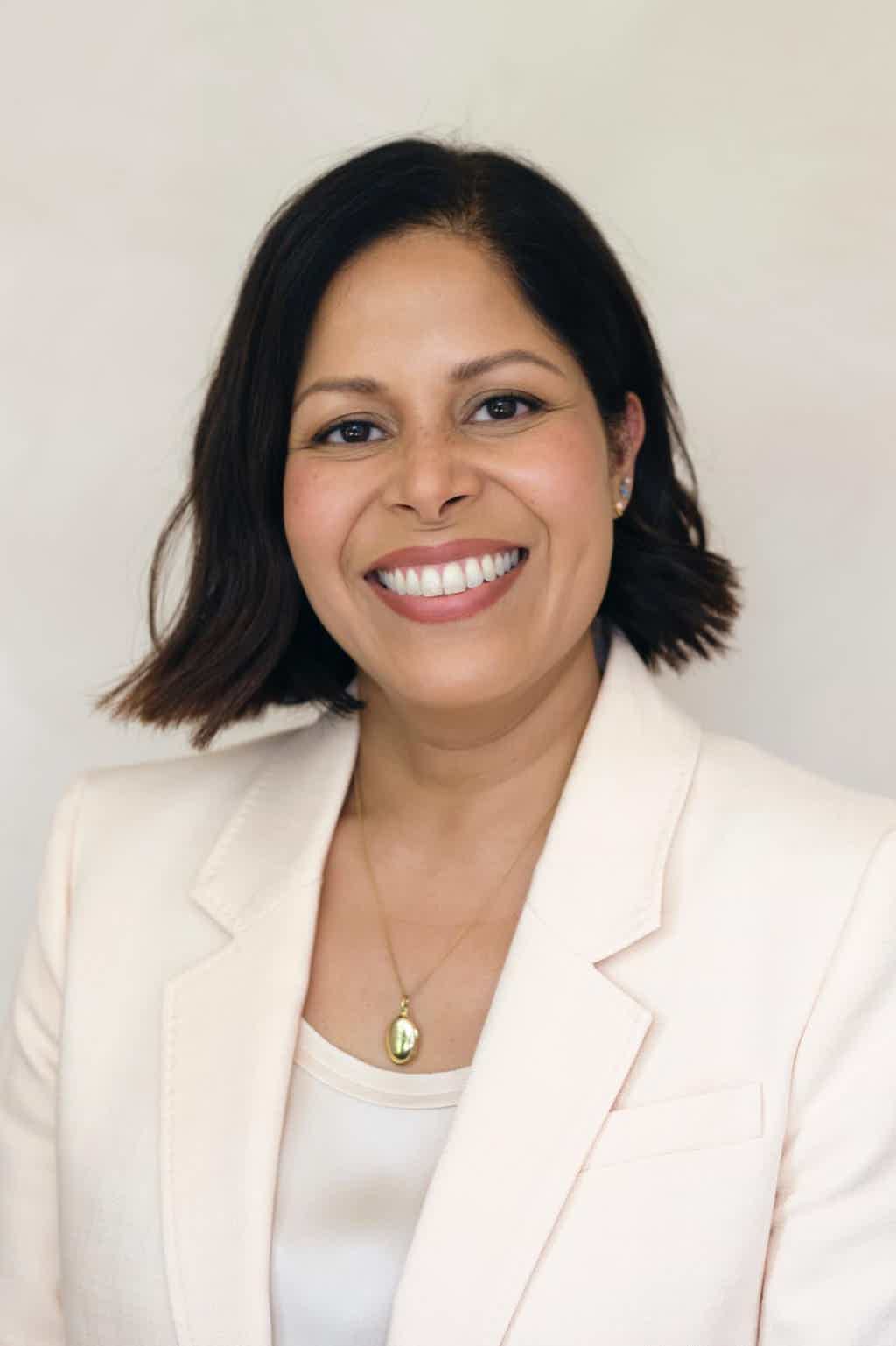 Woman in white blouse with long ponytail standing with arms open in a green forest.