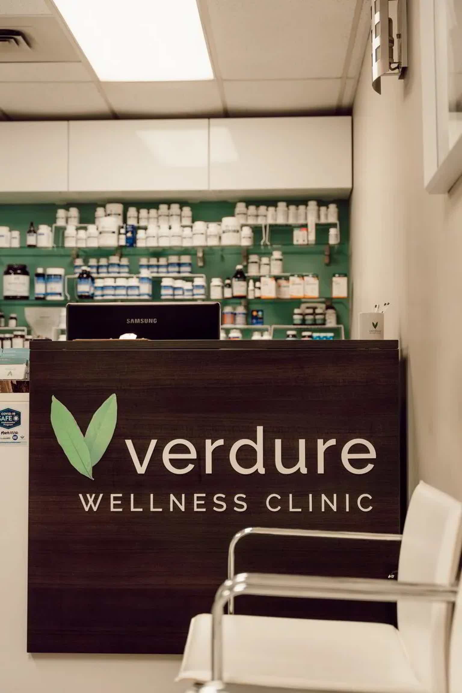VerDure Wellness Clinic reception desk with “verduur(e)” logo, medicine bottles and shelves in background.