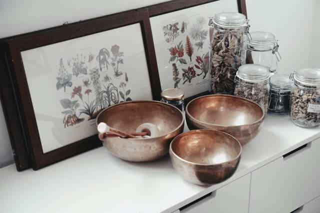 Copper bowls and jars on a white cabinet with framed botanical prints in the background.