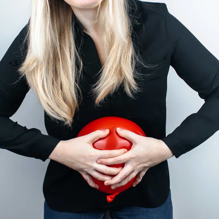 Person in black top holds a red deflated balloon against abdomen with both hands.