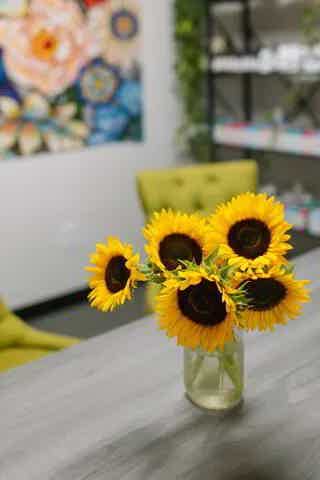 Sunflowers in a glass jar on a gray table, bright yellow petals and dark centers.