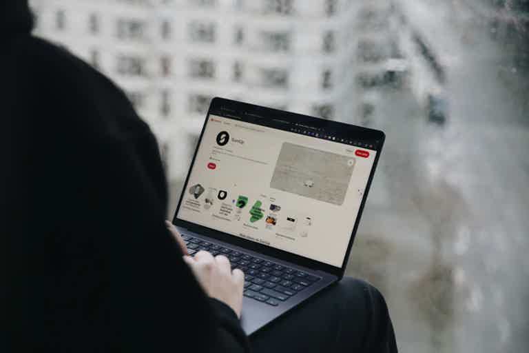 Person using a laptop near a window, screen shows a dashboard with graphs and tiles.