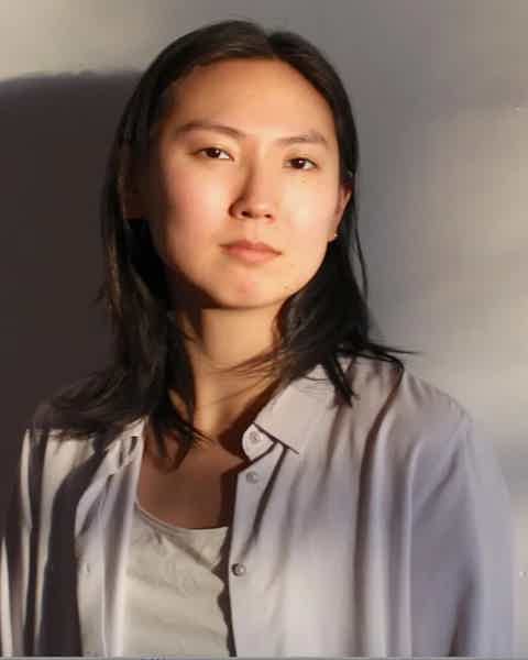 Portrait of a woman with shoulder-length dark hair, wearing a light shirt over a white top, neutral expression.