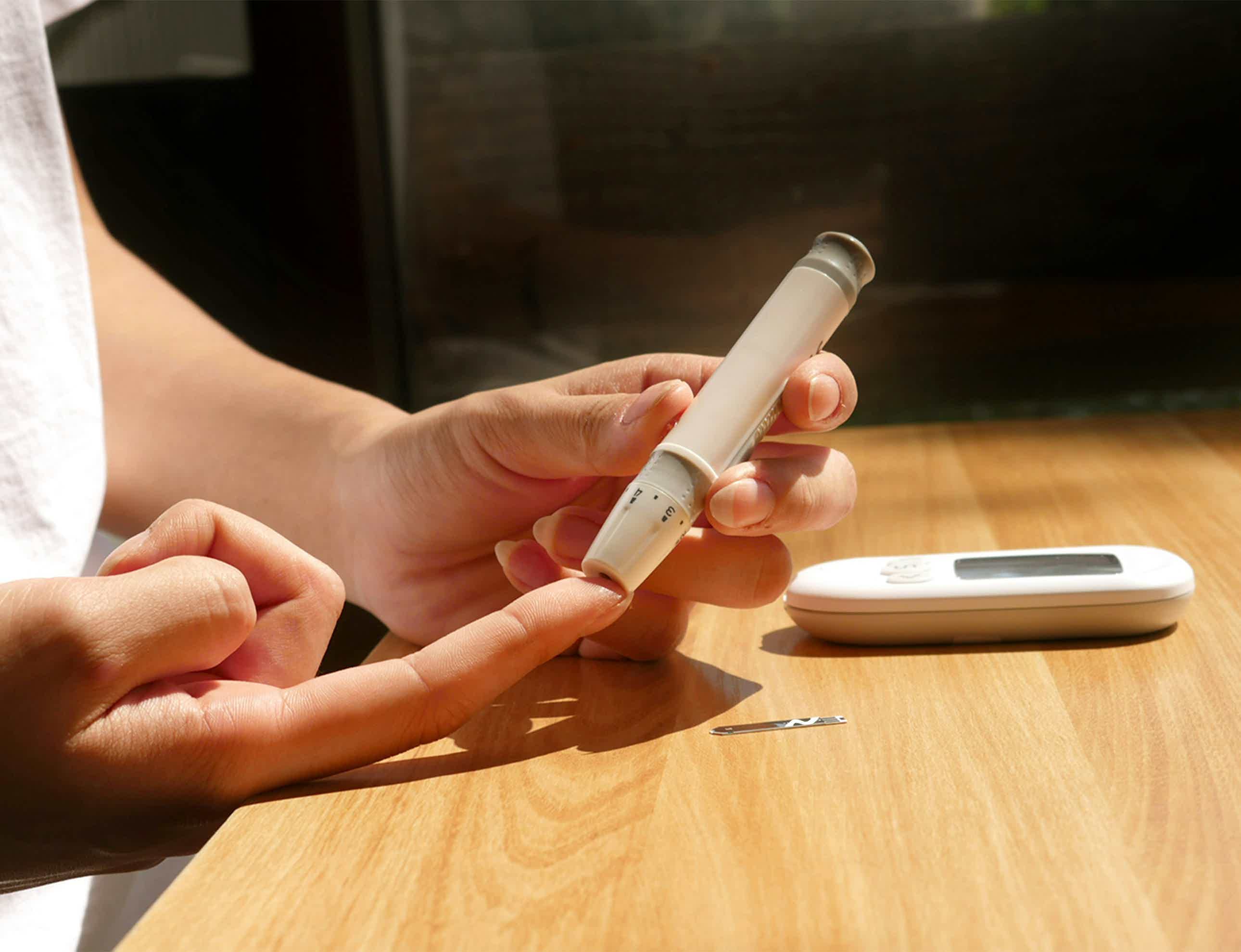Hand holding a white pen-like device with cartridge tip; healthcare device on wooden table.