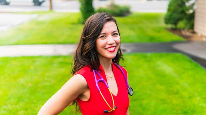 Dr. Kryzia Olsen in red dress with stethoscope, smiling outdoors.