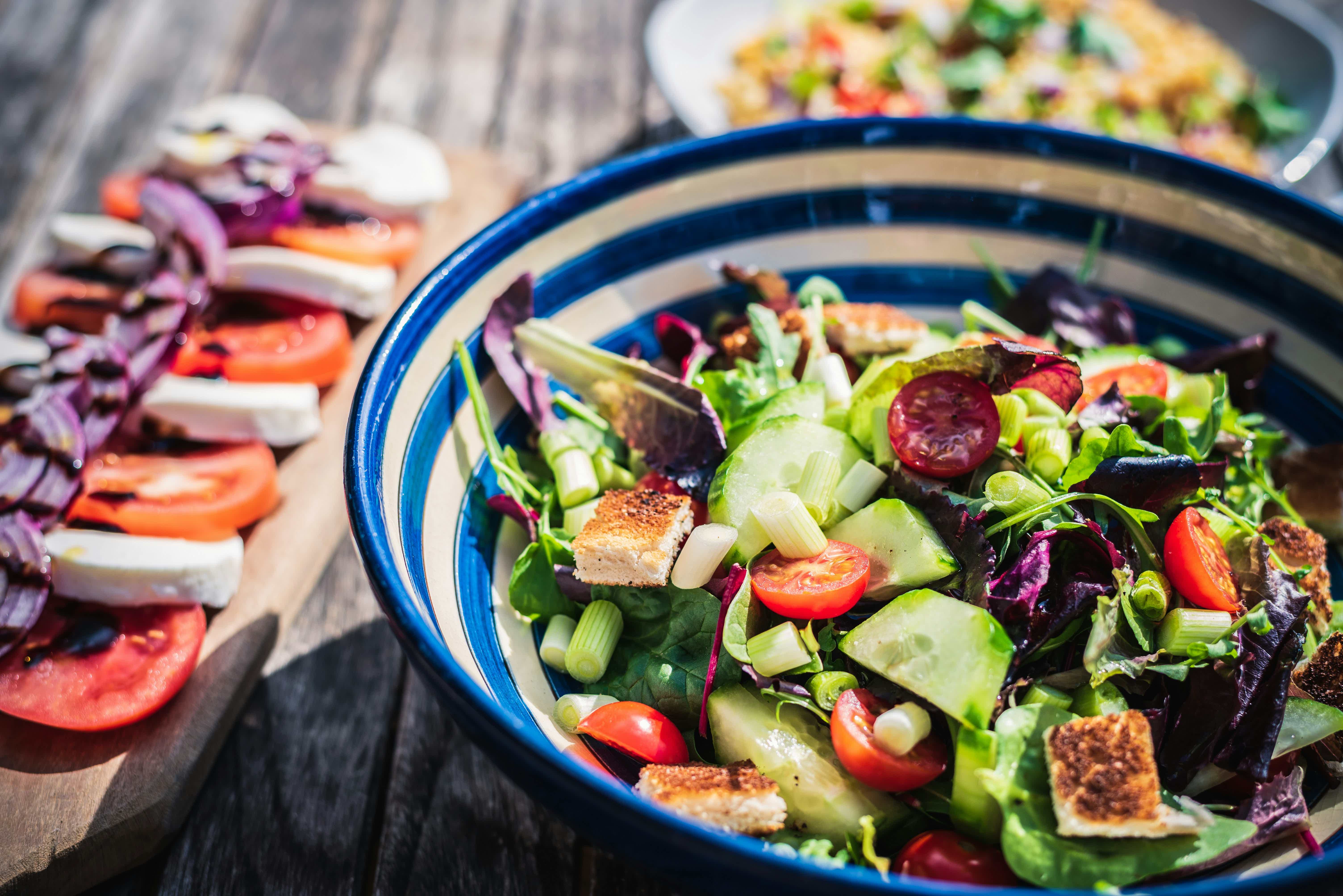 Large bowl of mixed salad greens with cucumbers, tomatoes, purple cabbage, and croutons on a wooden table.