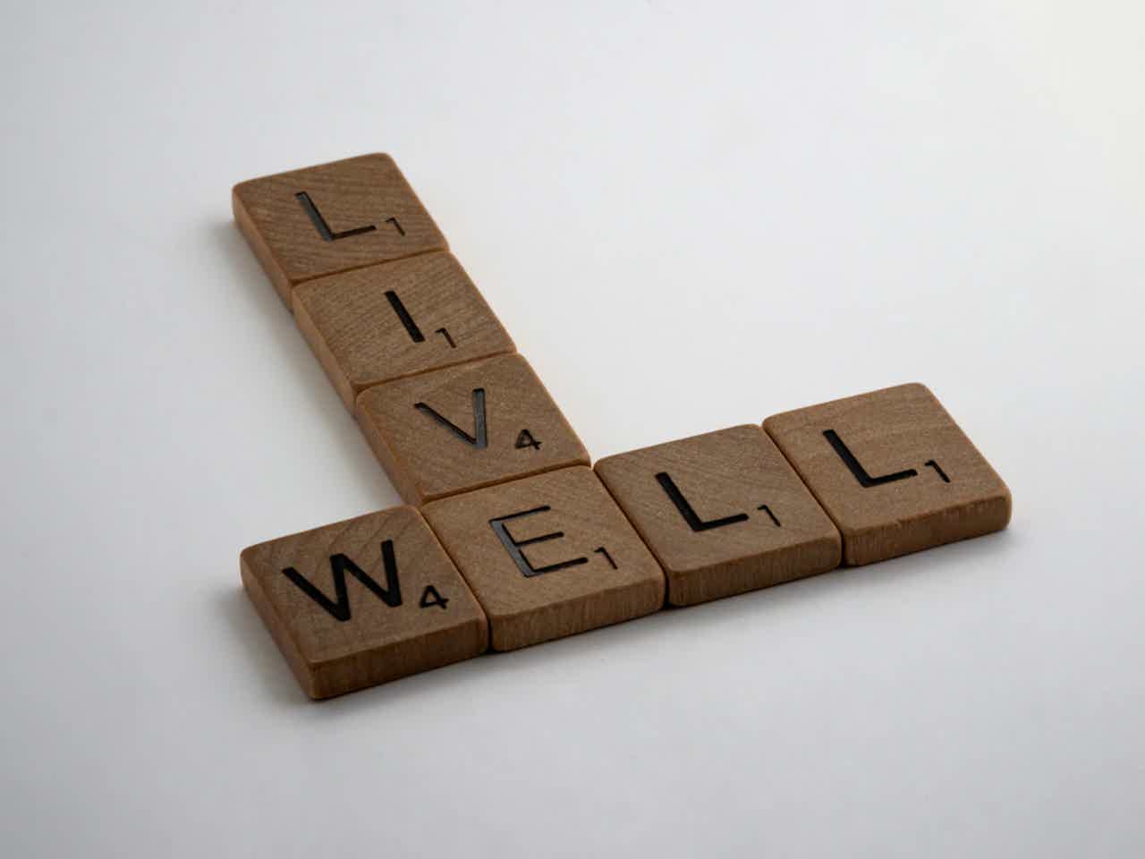 Scrabble-style wooden tiles spelling “WELL” with extra letters forming a vertical line.