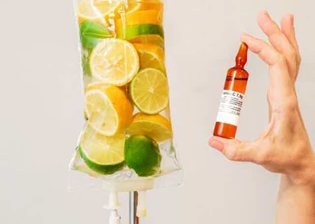 Hand holding small vial of vitamin C beside hanging fruit popsicle with citrus, lime, and green fruit.