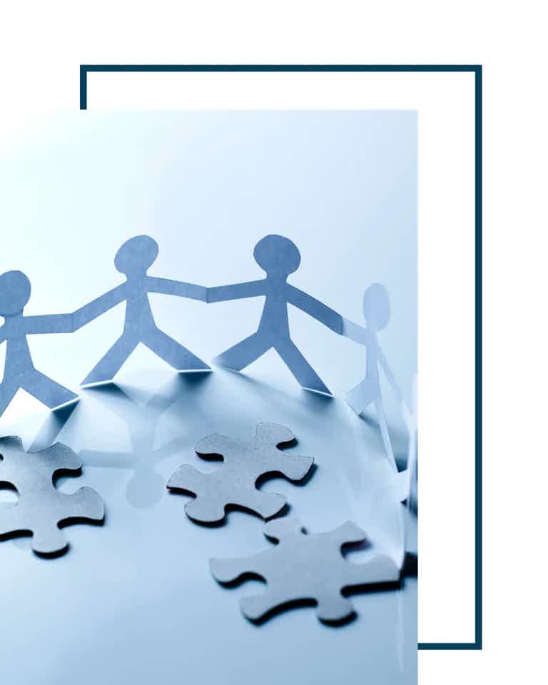 Linked paper chain of people holding hands around puzzle pieces, symbolizing teamwork and collaboration.