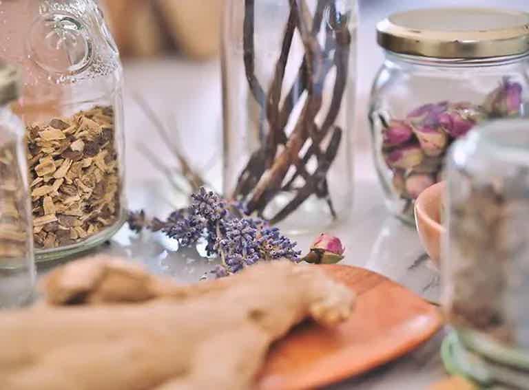 Dried herbs and flowers on a table with glass jars, suggesting an apothecary or natural healing setting.