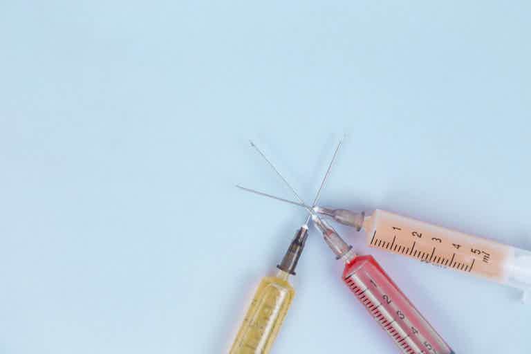Syringes with colored liquids arranged in a triangle on a light blue background.
