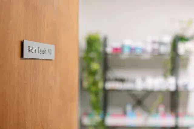 Door with nameplate “Robin Taziq MD” on wooden surface; blurred office shelves in background.