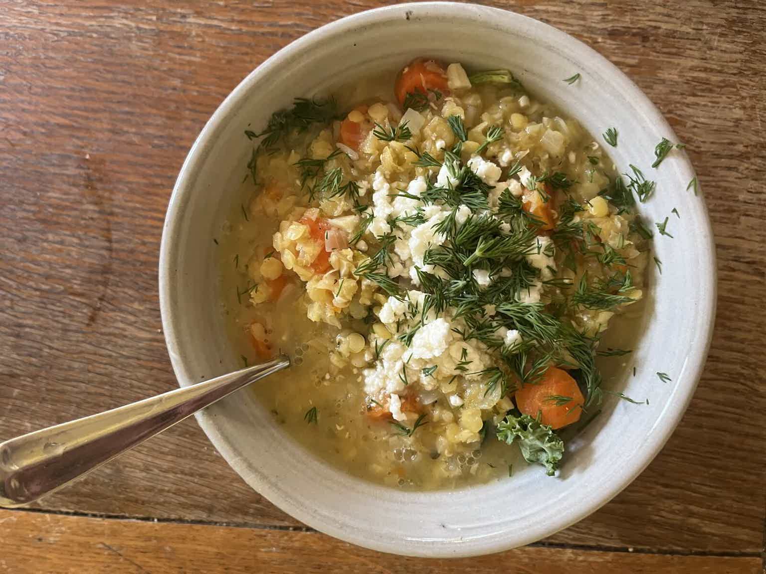 Creamy vegetable lentil soup with carrots, herbs, and crumbled cheese in a light broth.