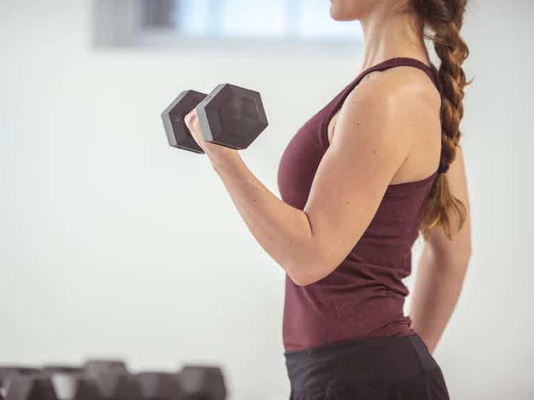 Woman in maroon tank top performs bicep curl with a dumbbell in a gym, focusing on arm workout.