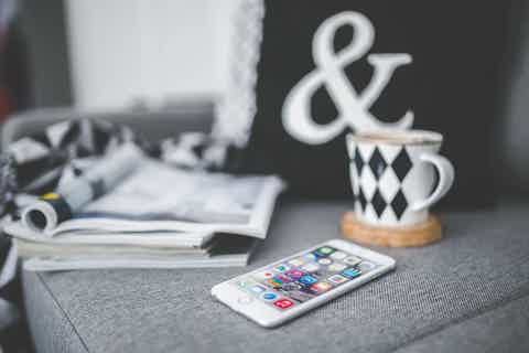 Ampersand sign with patterned mug on a gray table beside an open notebook and smartphone.