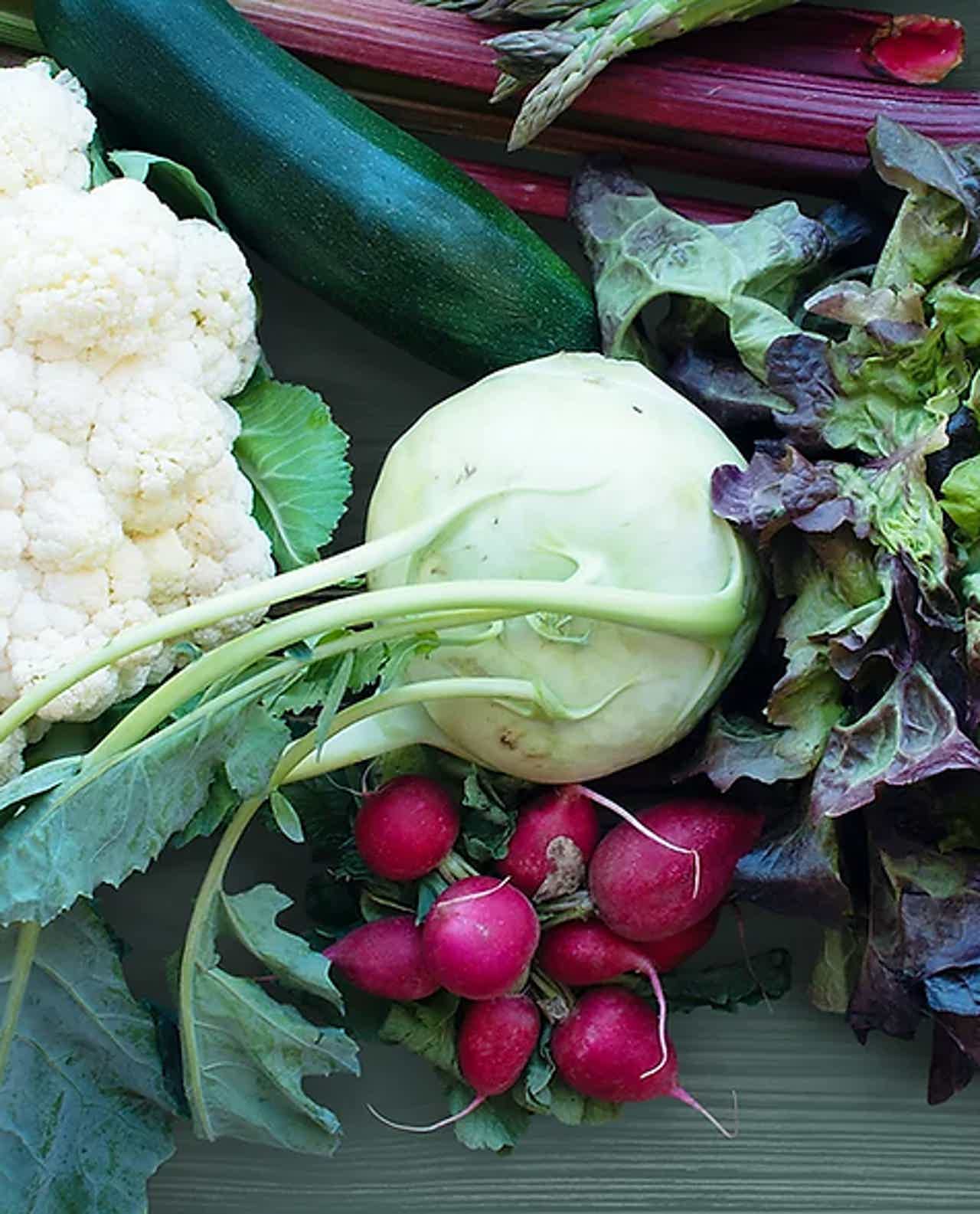 Assorted fresh vegetables including cauliflower, radishes, lettuce, and rhubarb on a wooden surface.
