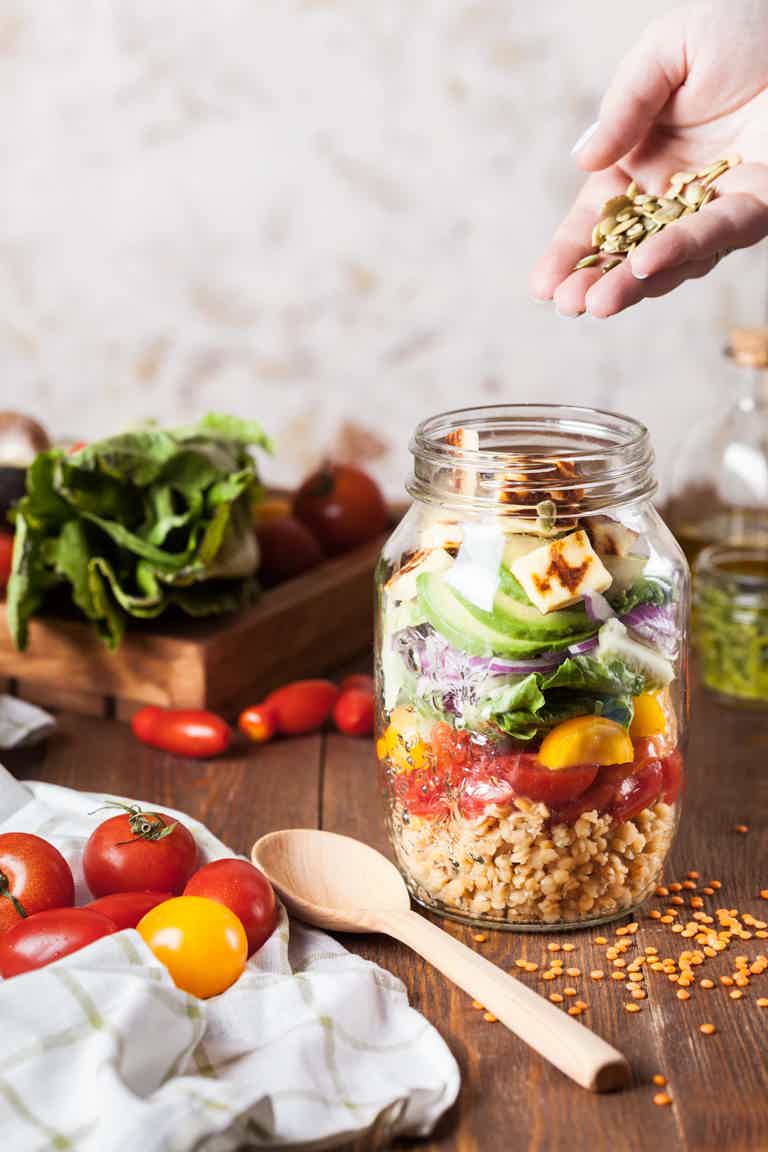 Layered salad in a jar on a wooden table with fresh ingredients around.