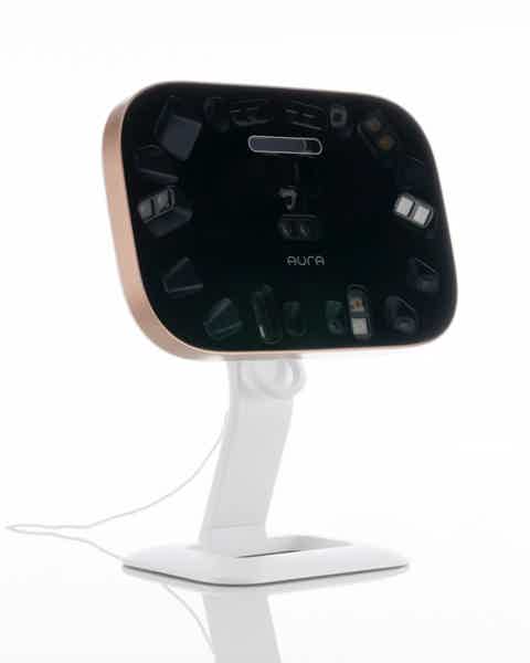 Small black facial device with multiple sensors on a white stand and gold trim. On white background.