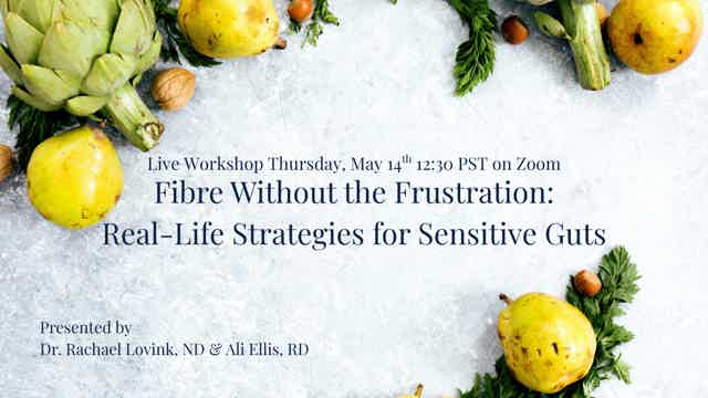 Smiling woman with blonde hair sits at desk, head resting on hand, brick wall and framed certificates in background.