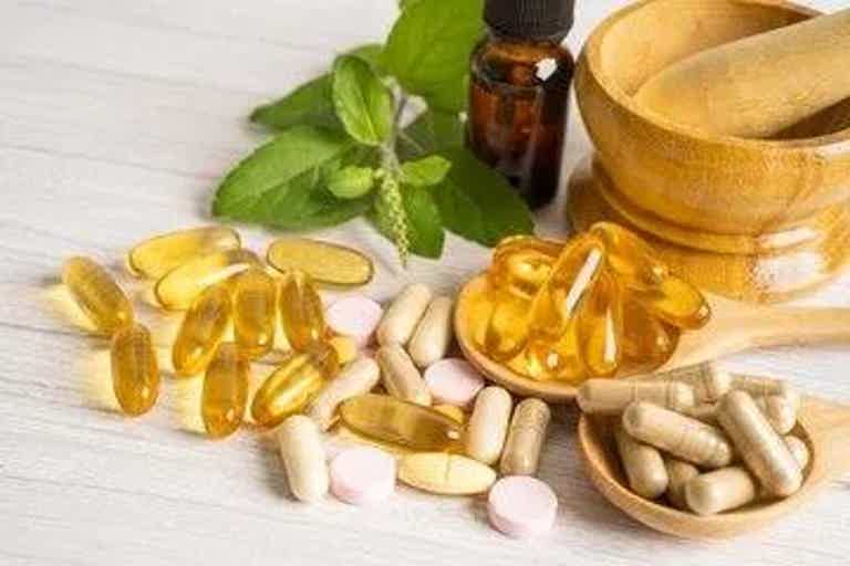 Assorted dietary supplements: yellow capsules, white pills, pink tablets, mortar and pestle, bottle, and fresh mint leaves.