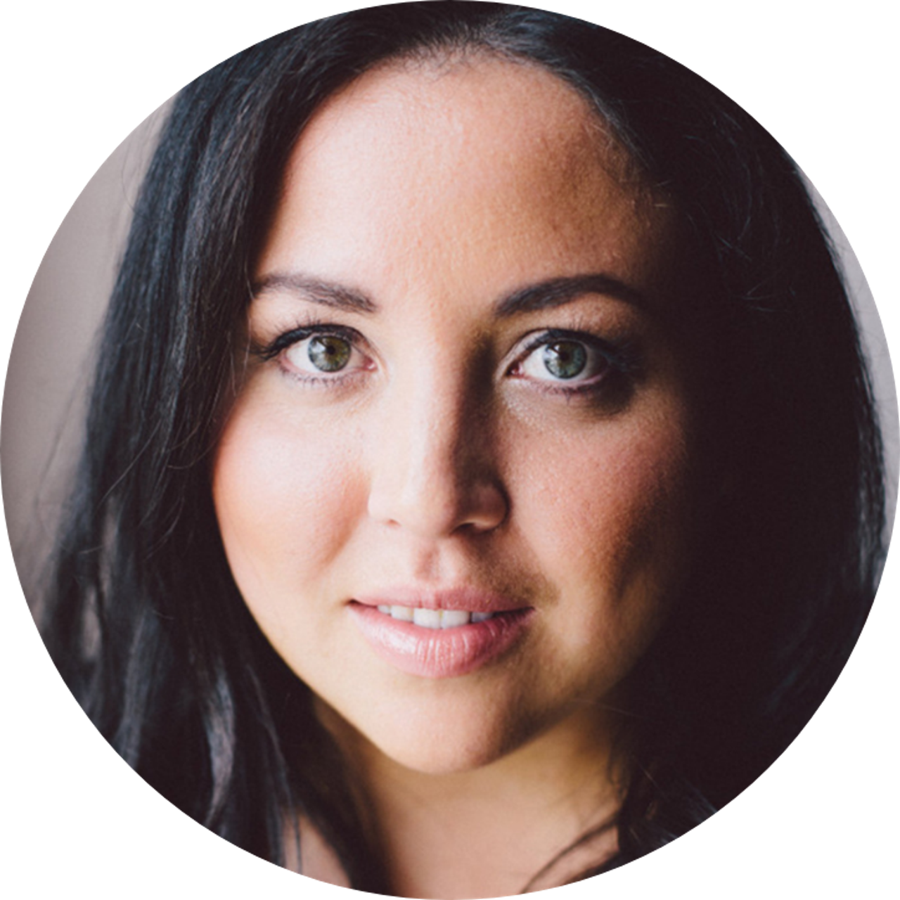 Smiling woman with blonde hair wearing a black wide-brim hat and black top, sitting against a dark backdrop.