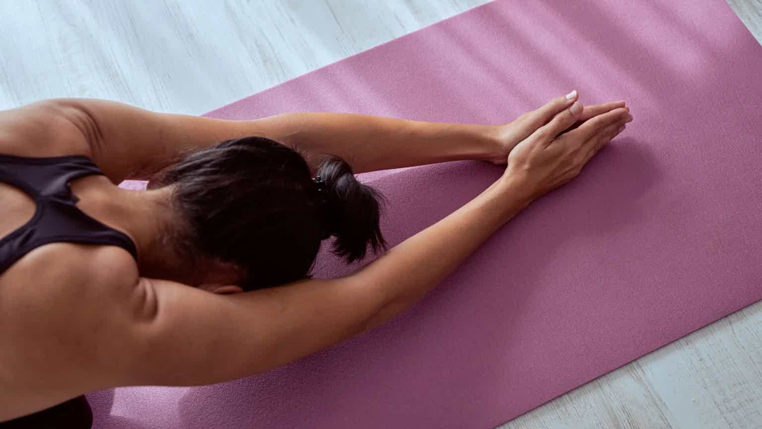 Person stretching on a purple yoga mat, lying on side with arms extended and head turned downward.