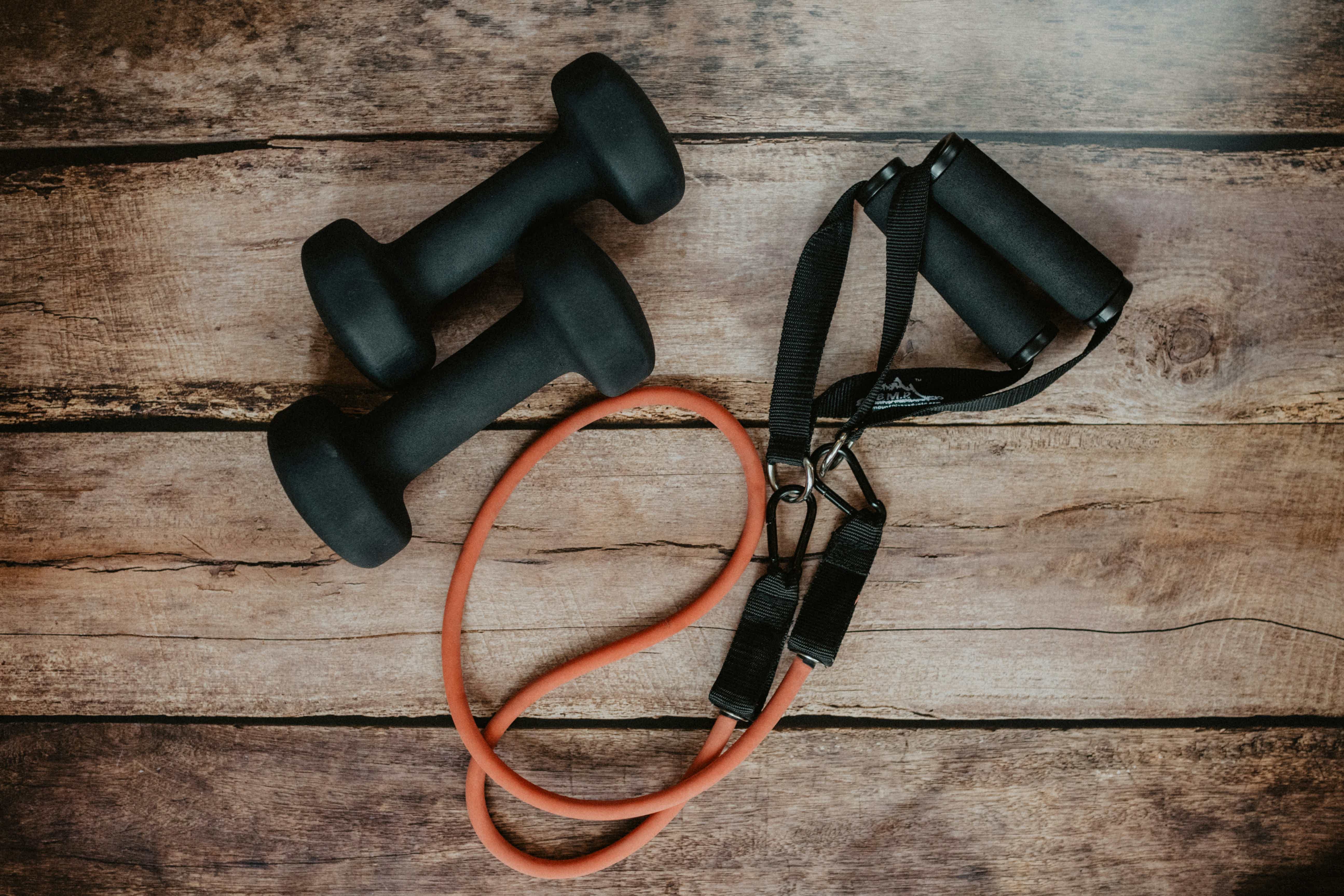 Two black dumbbells and an orange resistance band on a rustic wooden surface