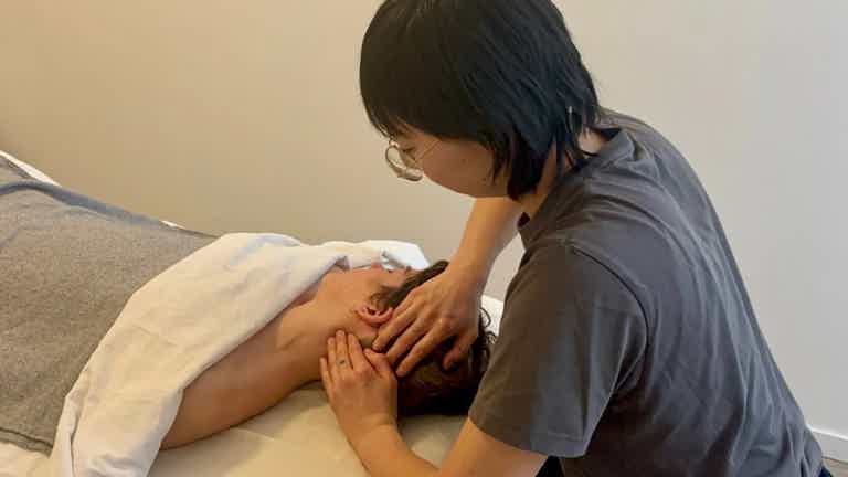 Massage Therapist performs assessment, gently holding a patient’s head.