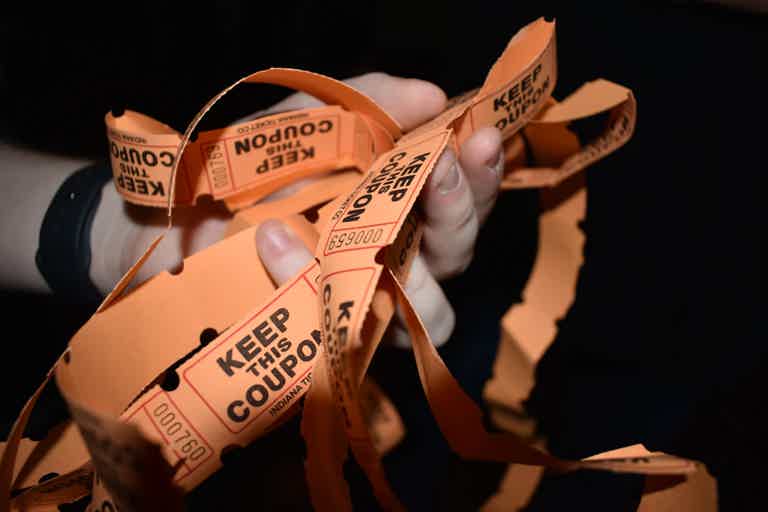 Crumpled orange coupons with “KEEP THIS COUPON” text, held by hands.