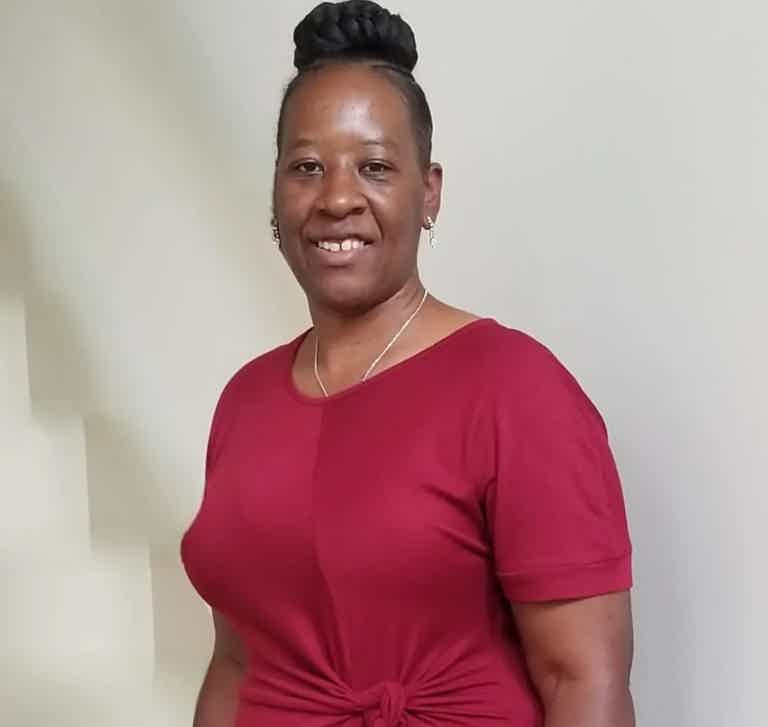 Woman in red short-sleeve top, tied at the waist, smiling, standing sideways in a light room.