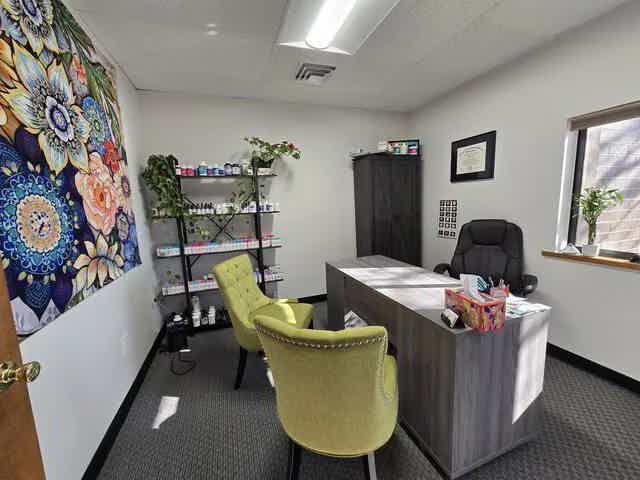 Naturopathic doctor's office with desk, two lime chairs, colorful wall tapestry, plant shelf, and window light in Denver
